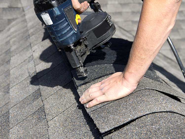 Roofer replacing missing shingles on roof.