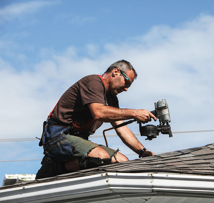 Roofer repairing a shingle roof using a nail gun.